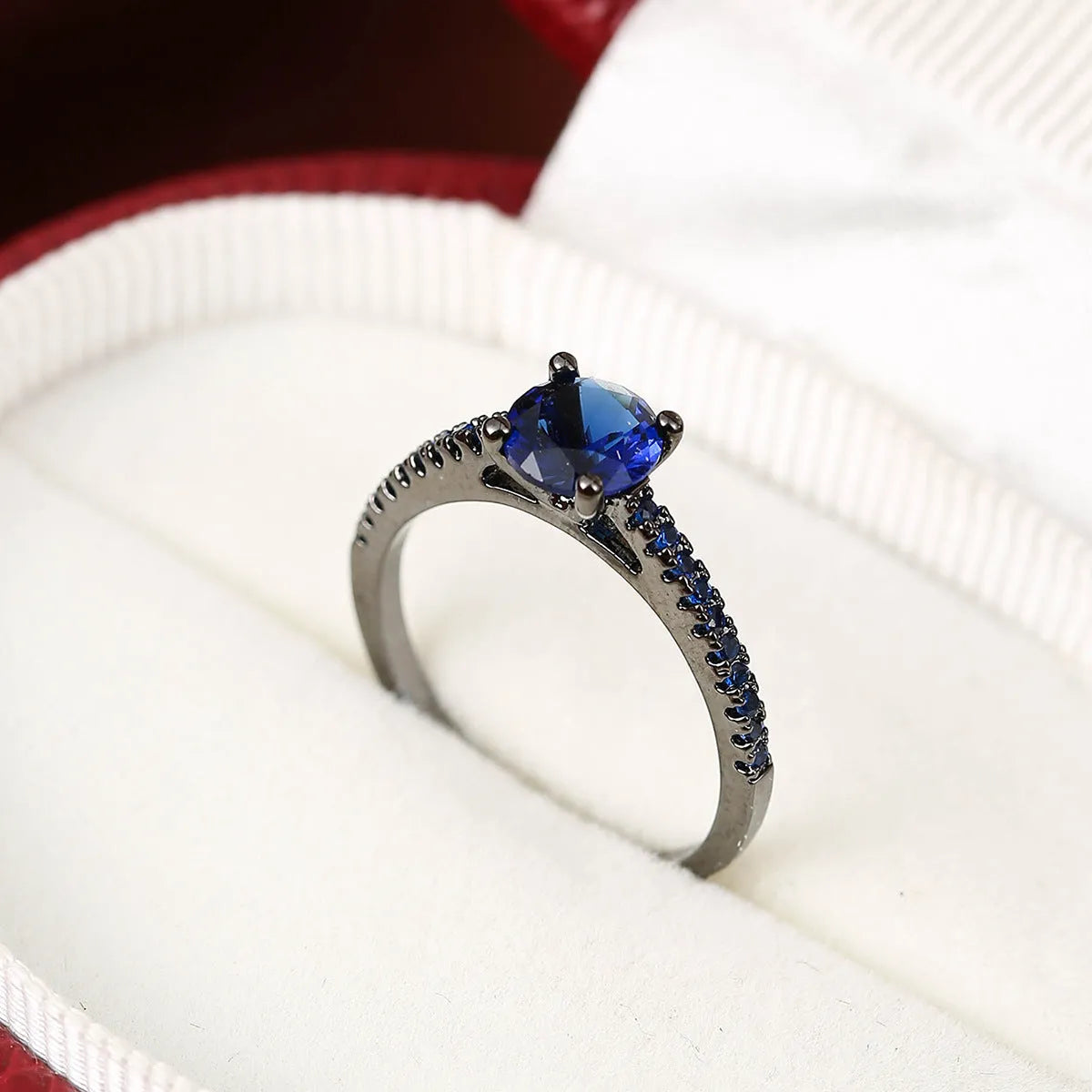 A hexagonal geometric ring with a zircon stone, shown in a gun black and rose red electroplated finish on a finger.