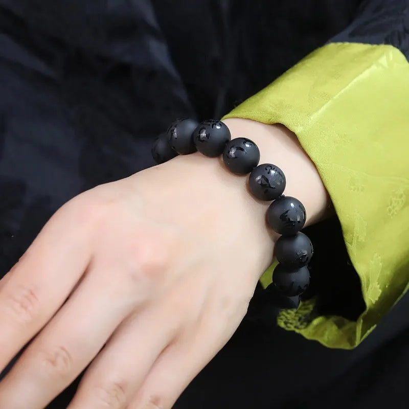 Close-up of a frosted black agate bracelet with Sanskrit mantra engraving on each bead, showing matte stone texture.