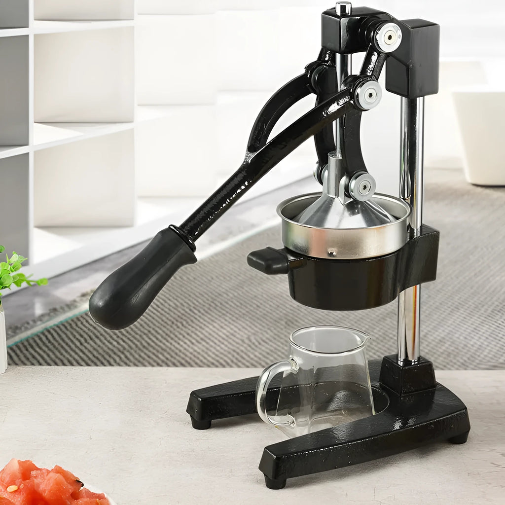Black cast iron manual citrus juicer with stainless steel funnel on a kitchen counter.