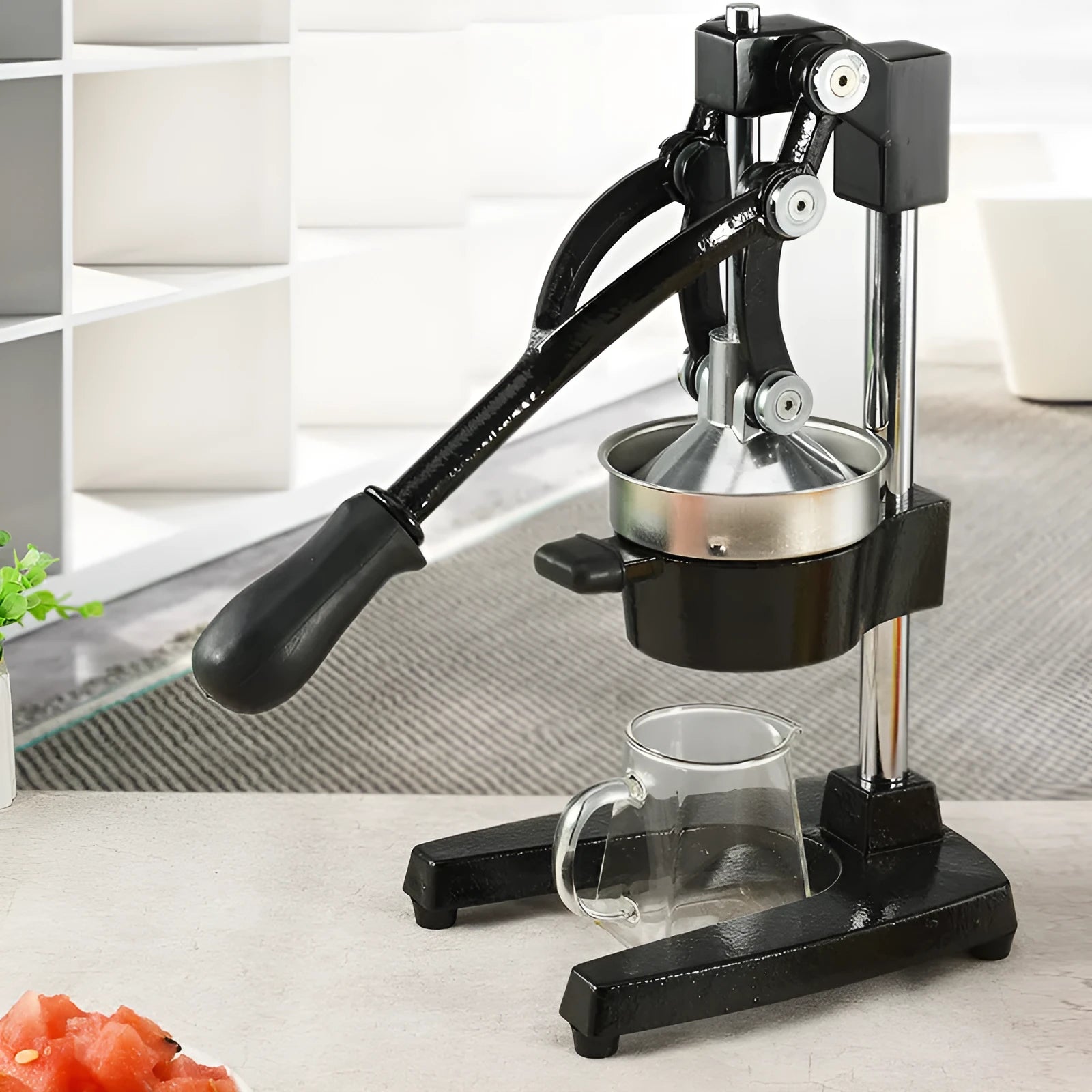 Black cast iron manual citrus juicer with stainless steel funnel on a kitchen counter.