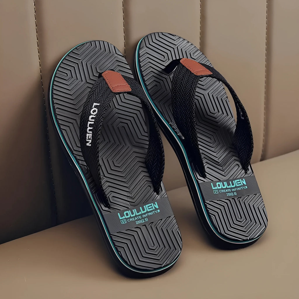 Men's black flip flops with open toe design and textured non-slip sole on a sandy beach.