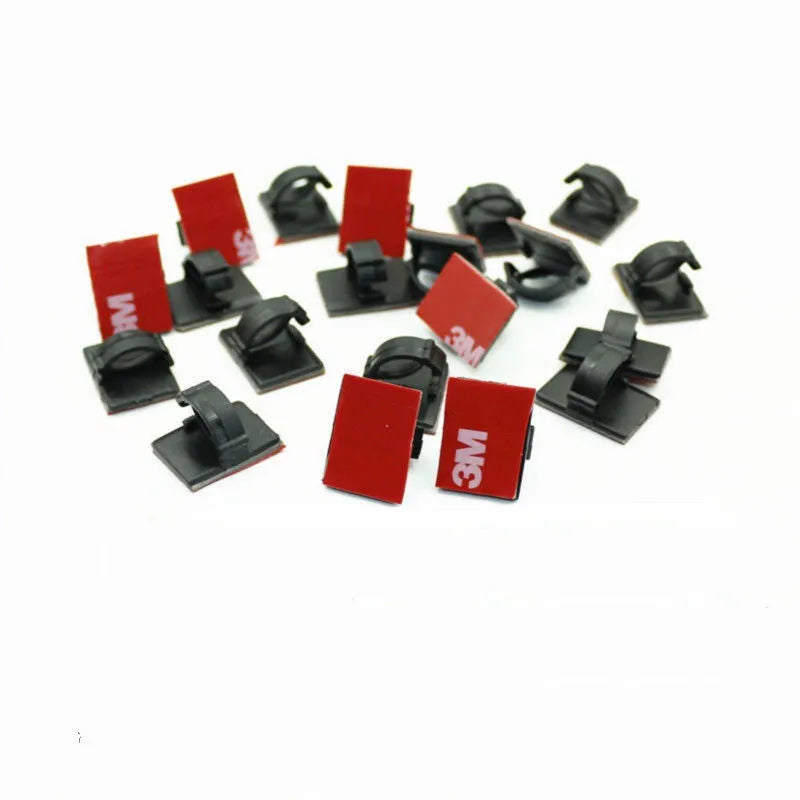 Black and white plastic self-adhesive wire clamps for organising flat cables on a surface.