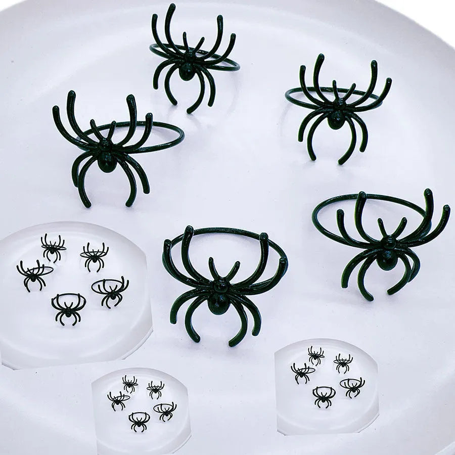 Six black alloy spider-shaped napkin rings for Halloween table decoration on a dark tablecloth.