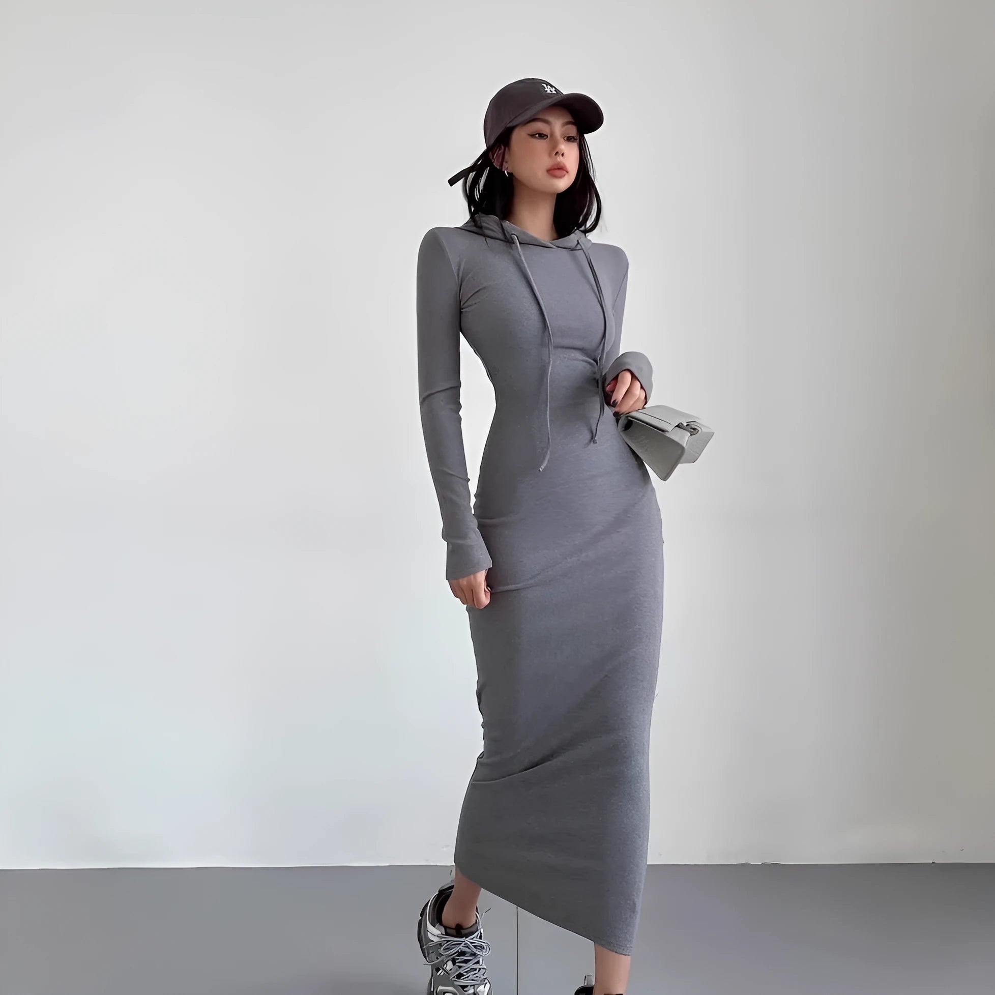 A woman modelling a grey hooded long-sleeve sheath dress with a high waist and over-the-knee length.