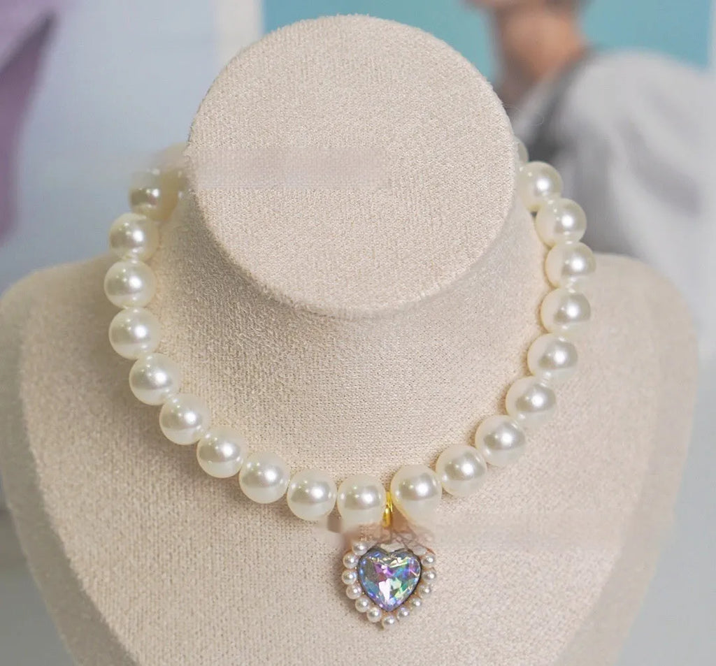 Pearl necklace cat collar with heart-shaped gem charm in various colours on a white background.