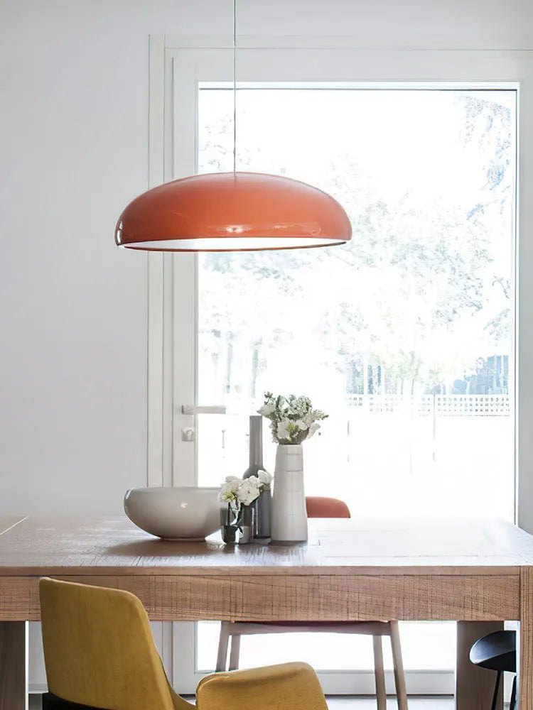 Orange iron Danish-style pendant lamp with adjustable cable above a restaurant table.