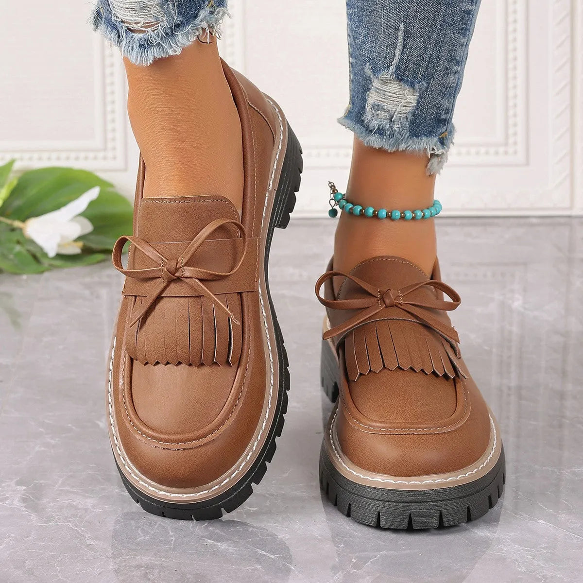 Black plus size women's loafers with tassel trim and a bowknot on a chunky rubber sole.