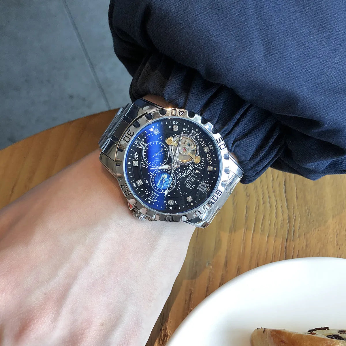 Men's silver automatic mechanical watch with black dial, luminous hands, on a black steel strap.