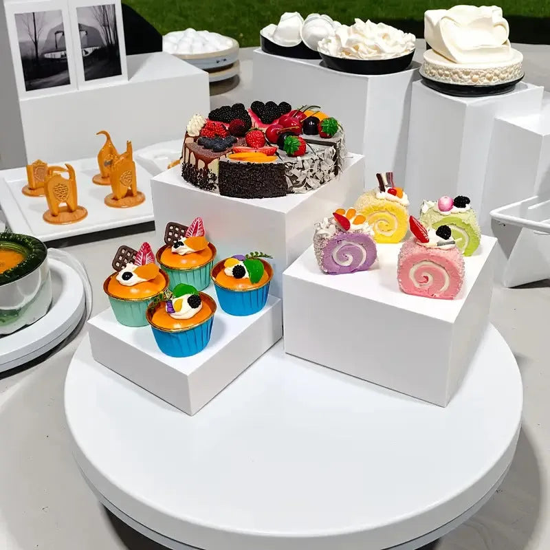 Set of six white plastic stacking cubes for displaying cakes and desserts on a table.