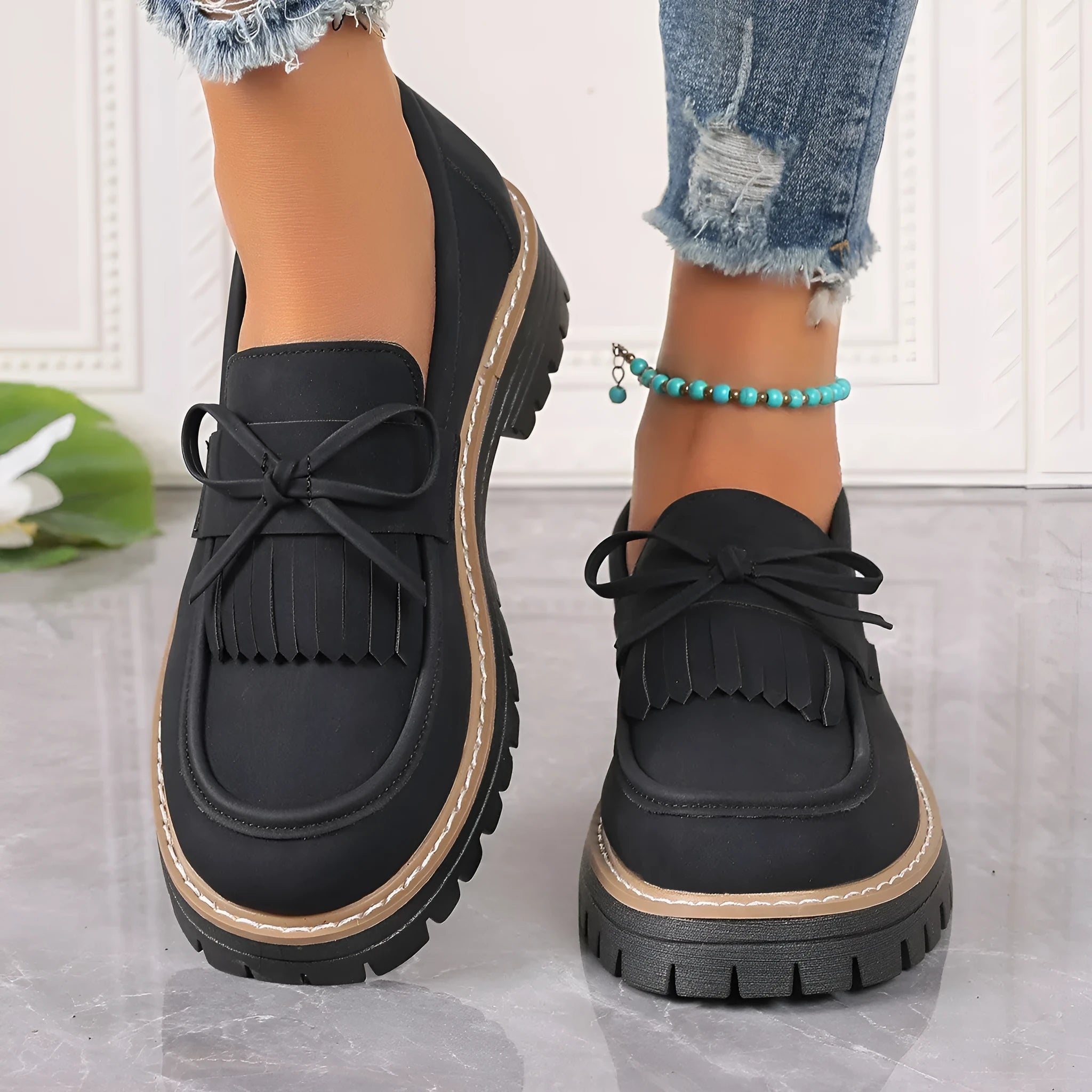 Black plus size women's loafers with tassel trim and a bowknot on a chunky rubber sole.