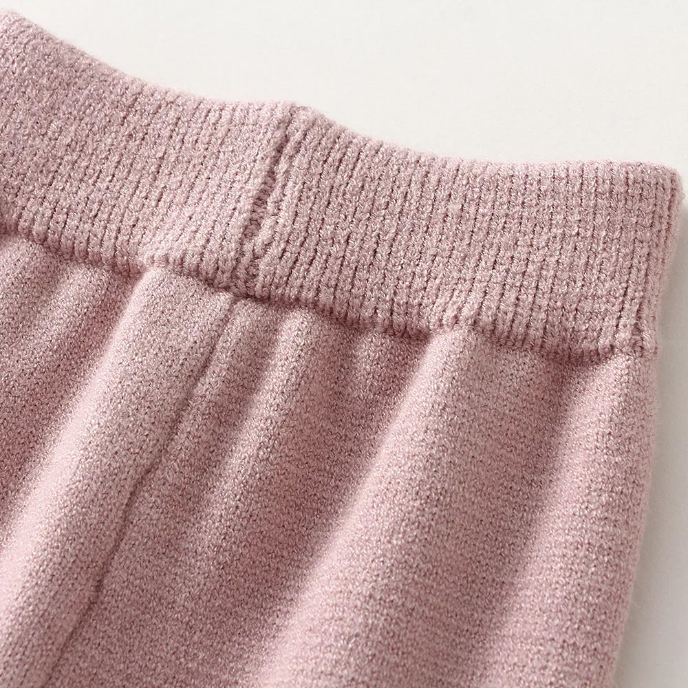 Baby girl wearing a pink knitted pullover sweater and matching trousers set.