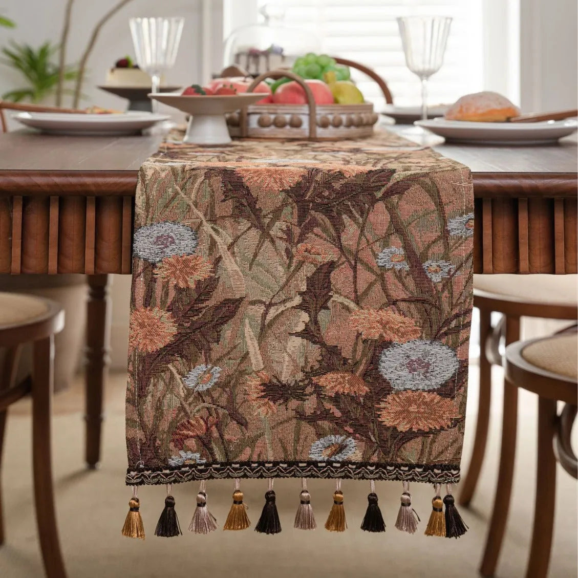 Beige jacquard table runner with flower pattern and long tassels on a wooden dining table.