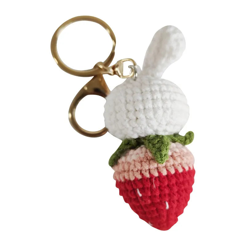 Close-up of a white hand-woven wire pendant showing a rabbit and strawberry cartoon design on a key ring.