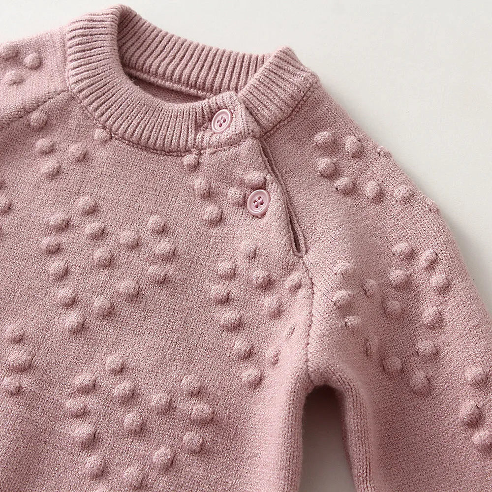 Baby girl wearing a pink knitted pullover sweater and matching trousers set.