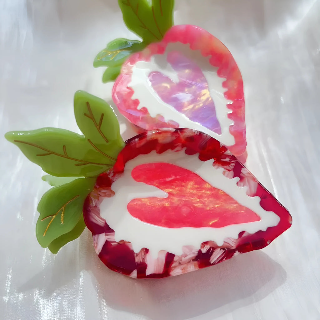 Close-up of a handmade red and pink strawberry hairpin on a pastoral background.