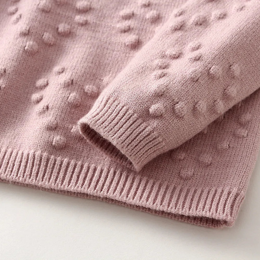 Baby girl wearing a pink knitted pullover sweater and matching trousers set.