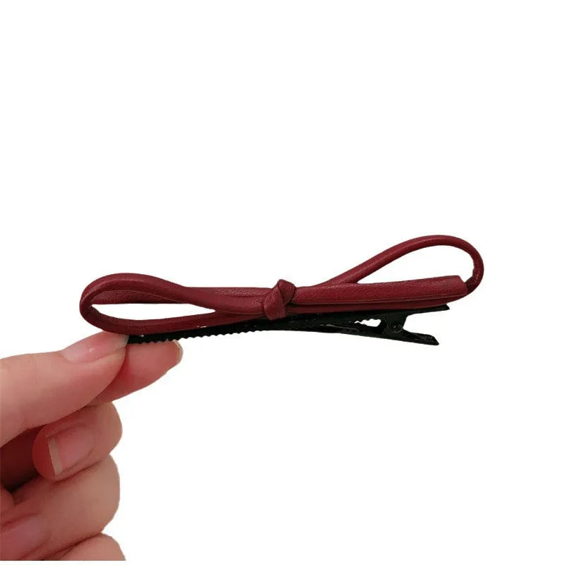 Handmade wine red leather bow hair clip on a 7cm metal alligator clip, shown on dark hair.