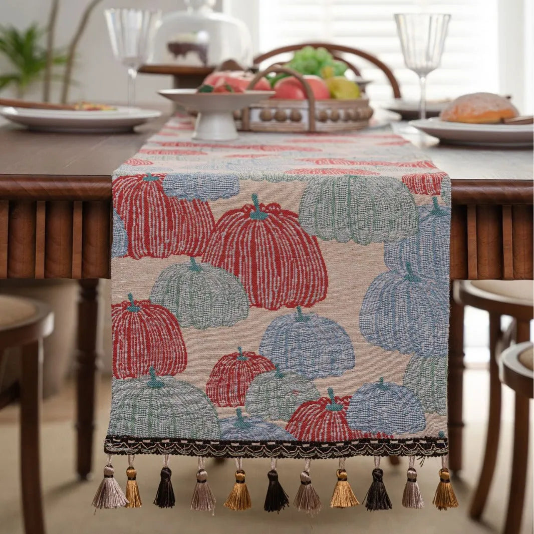 Beige jacquard table runner with flower pattern and long tassels on a wooden dining table.