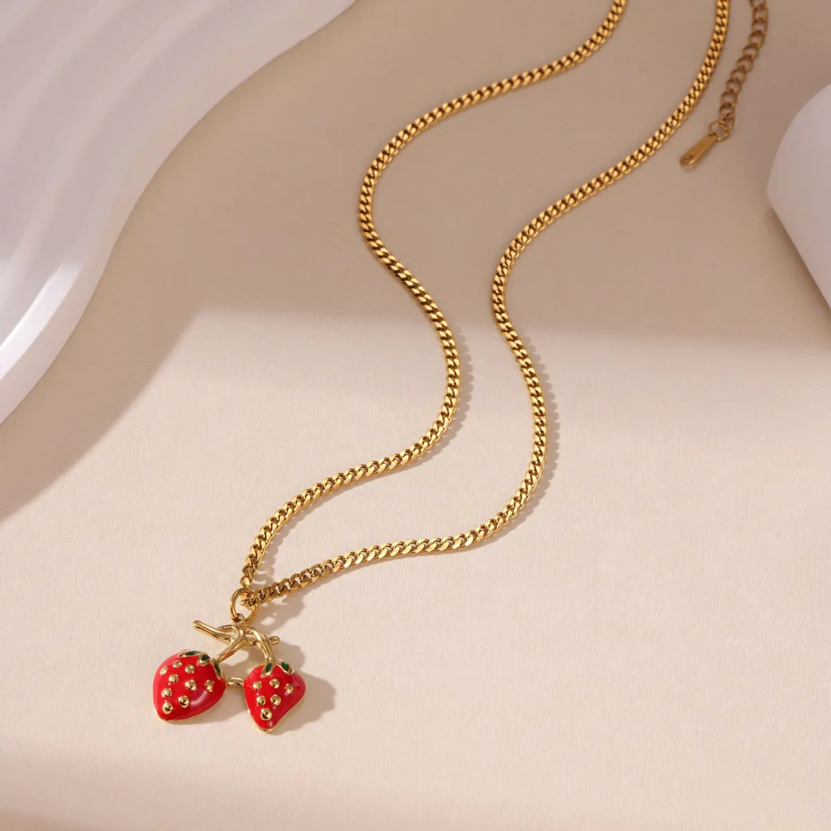 A women's necklace with a detailed strawberry-shaped alloy pendant on a stainless steel chain, shown in red and white gradient colour options.