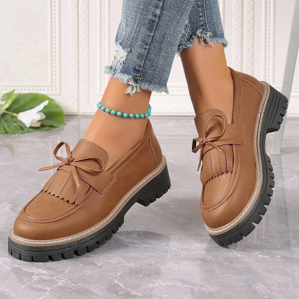 Black plus size women's loafers with tassel trim and a bowknot on a chunky rubber sole.