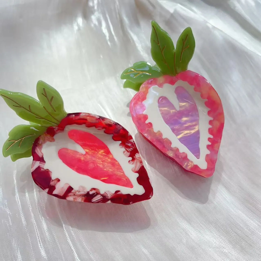 Close-up of a handmade red and pink strawberry hairpin on a pastoral background.