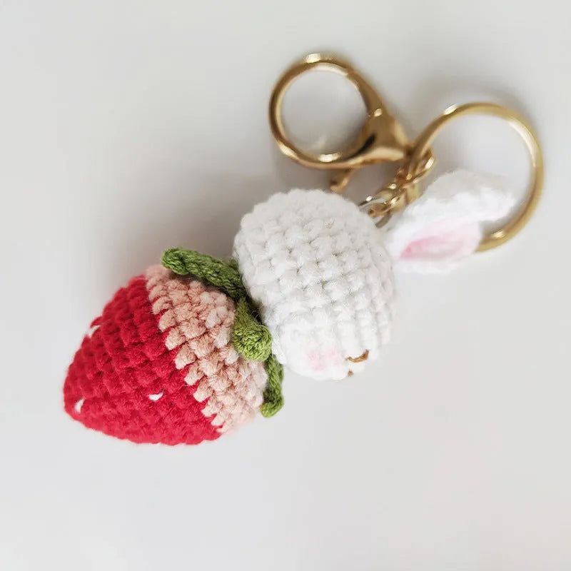 Close-up of a white hand-woven wire pendant showing a rabbit and strawberry cartoon design on a key ring.