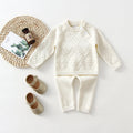 Baby girl wearing a pink knitted pullover sweater and matching trousers set.