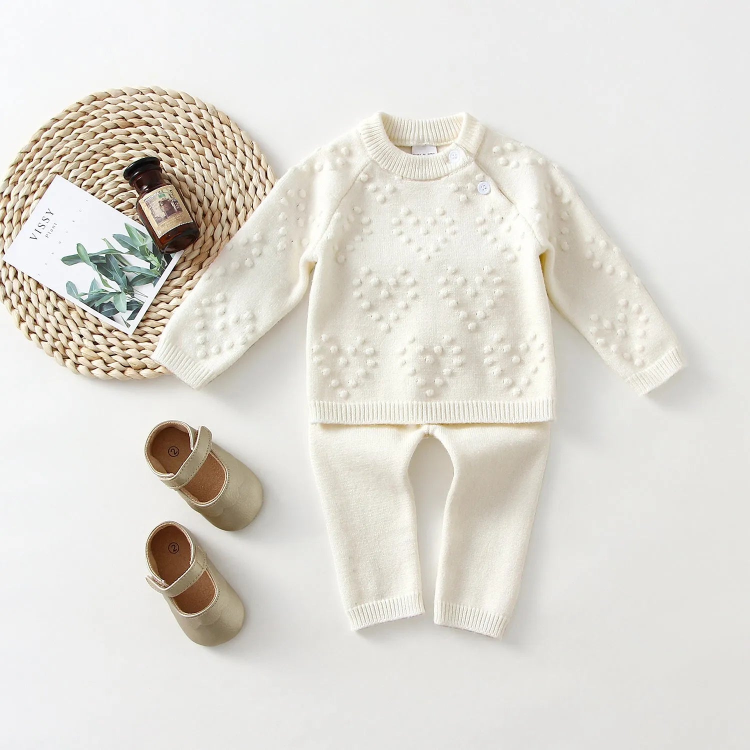 Baby girl wearing a pink knitted pullover sweater and matching trousers set.