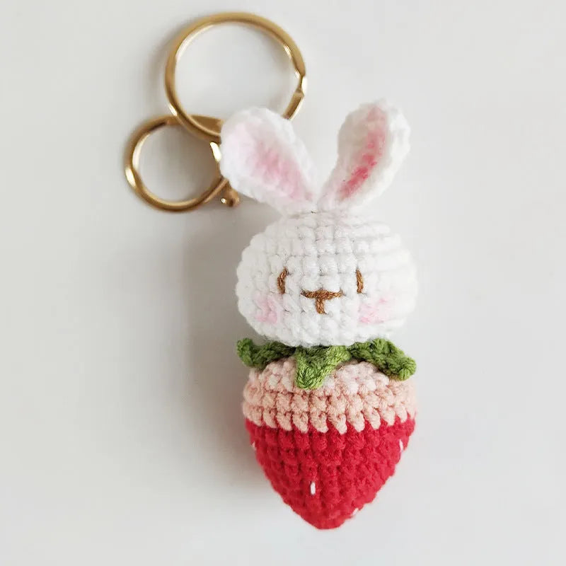 Close-up of a white hand-woven wire pendant showing a rabbit and strawberry cartoon design on a key ring.