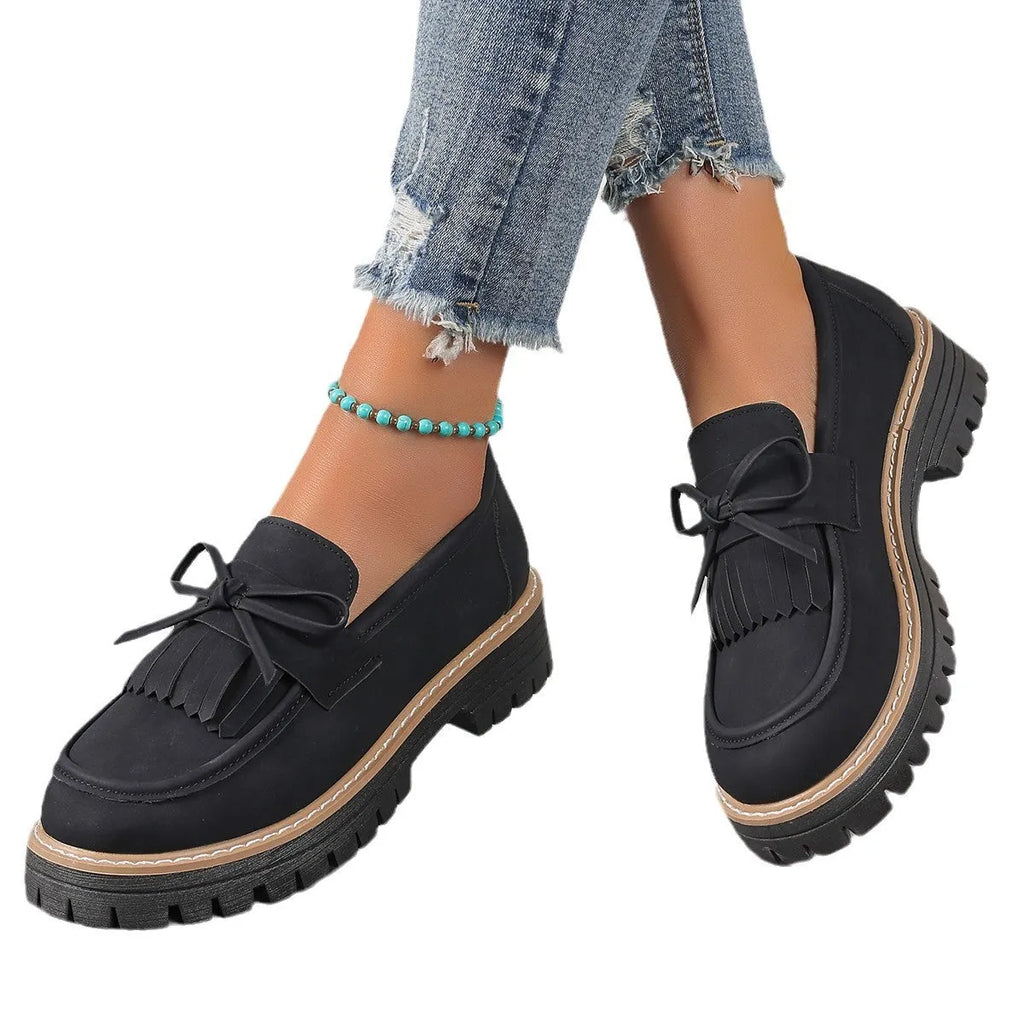 Black plus size women's loafers with tassel trim and a bowknot on a chunky rubber sole.