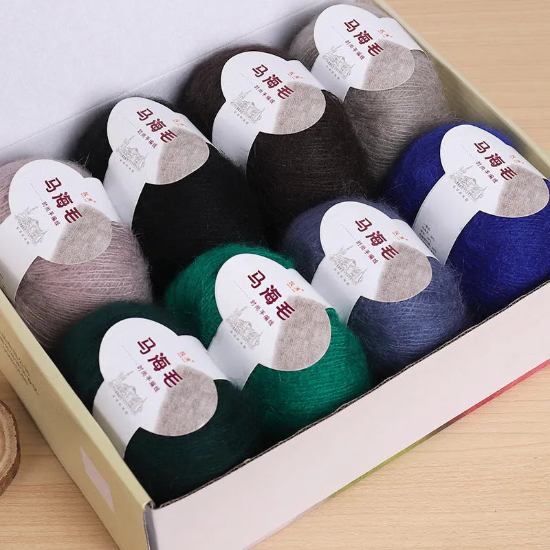 Single 100g ball of mohair yarn in a chosen colour next to a hand-woven light grey scarf sample.