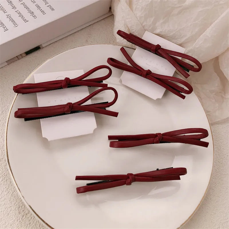 Handmade wine red leather bow hair clip on a 7cm metal alligator clip, shown on dark hair.