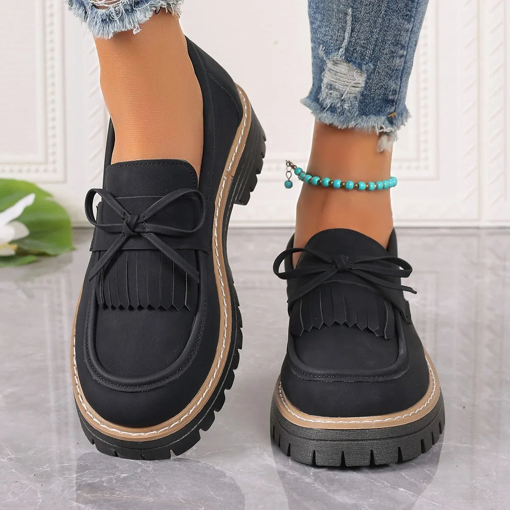 Black plus size women's loafers with tassel trim and a bowknot on a chunky rubber sole.