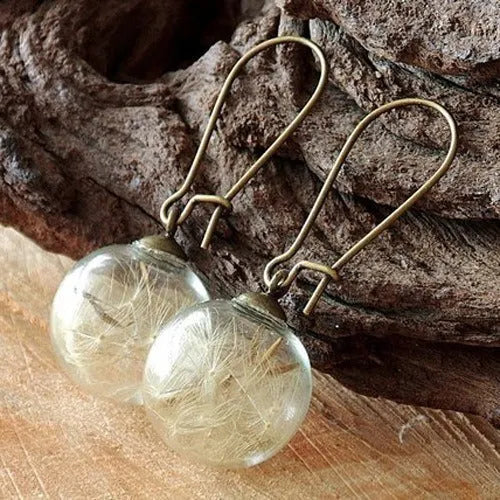 Close-up of transparent glass ball earrings showing a crystal dandelion seed design inside, with silver French hook.