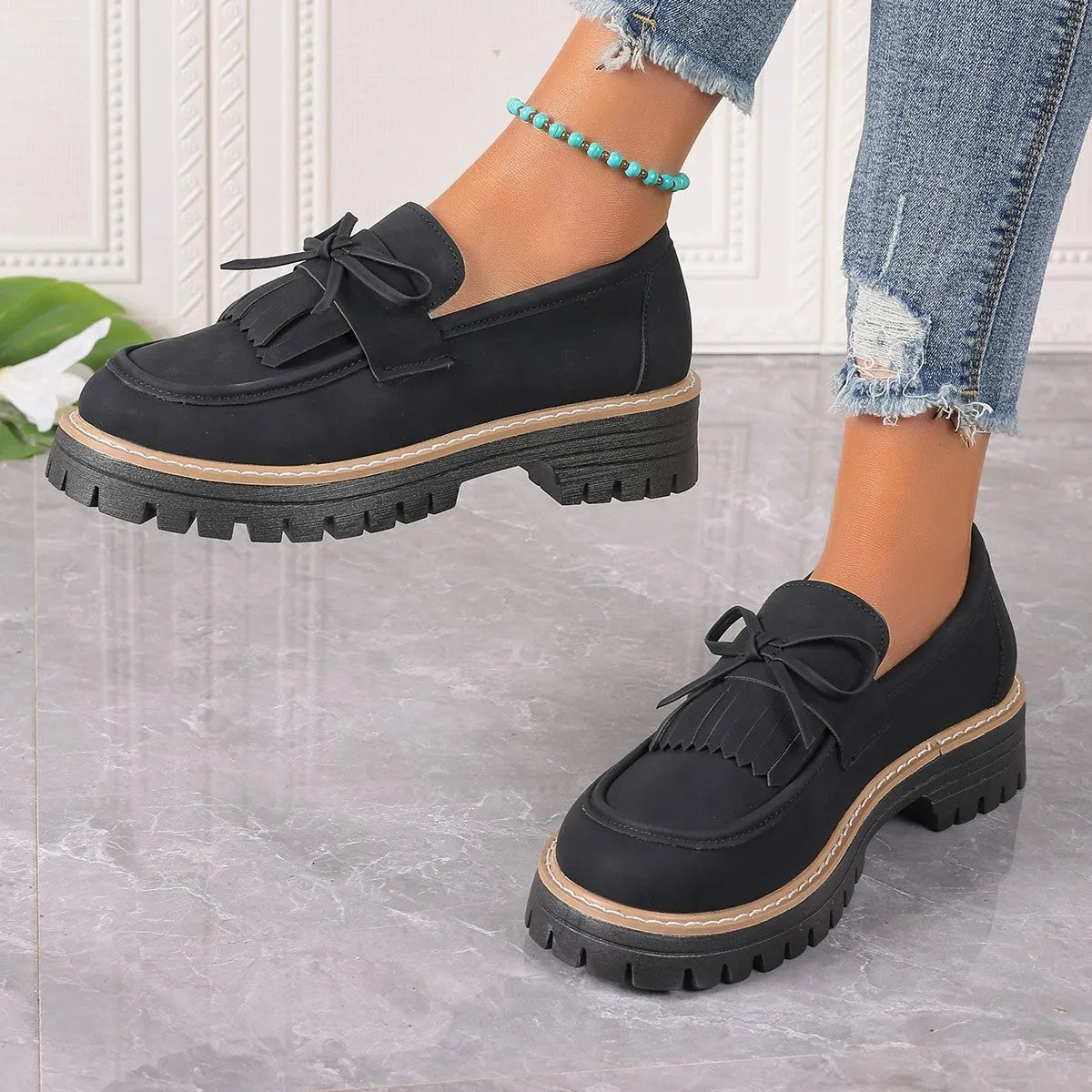 Black plus size women's loafers with tassel trim and a bowknot on a chunky rubber sole.