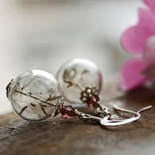 Close-up of transparent glass ball earrings showing a crystal dandelion seed design inside, with silver French hook.