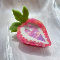 Close-up of a handmade red and pink strawberry hairpin on a pastoral background.