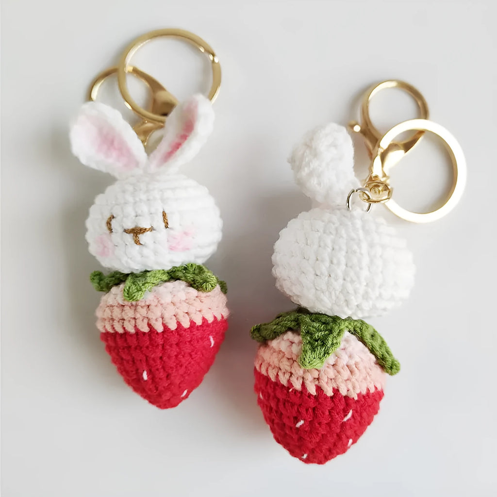 Close-up of a white hand-woven wire pendant showing a rabbit and strawberry cartoon design on a key ring.