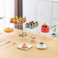 Set of six white plastic stacking cubes for displaying cakes and desserts on a table.