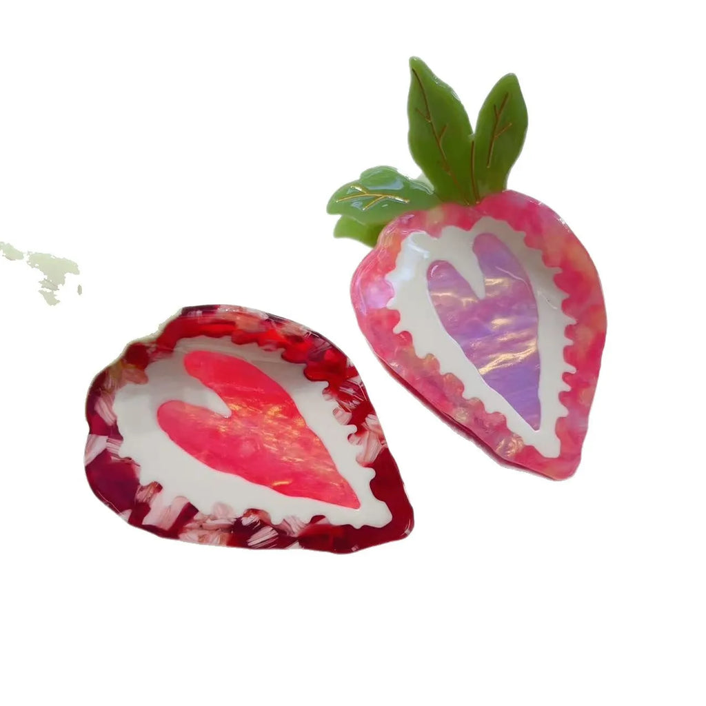 Close-up of a handmade red and pink strawberry hairpin on a pastoral background.