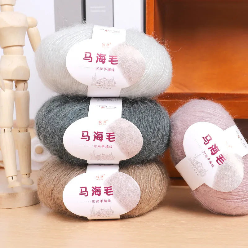 Single 100g ball of mohair yarn in a chosen colour next to a hand-woven light grey scarf sample.