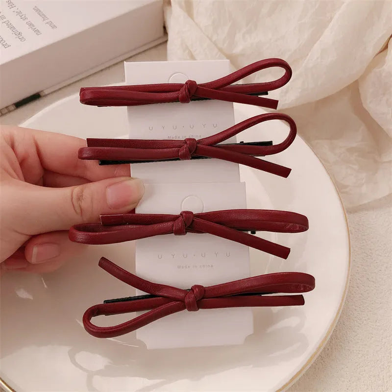 Handmade wine red leather bow hair clip on a 7cm metal alligator clip, shown on dark hair.