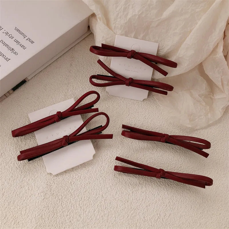 Handmade wine red leather bow hair clip on a 7cm metal alligator clip, shown on dark hair.