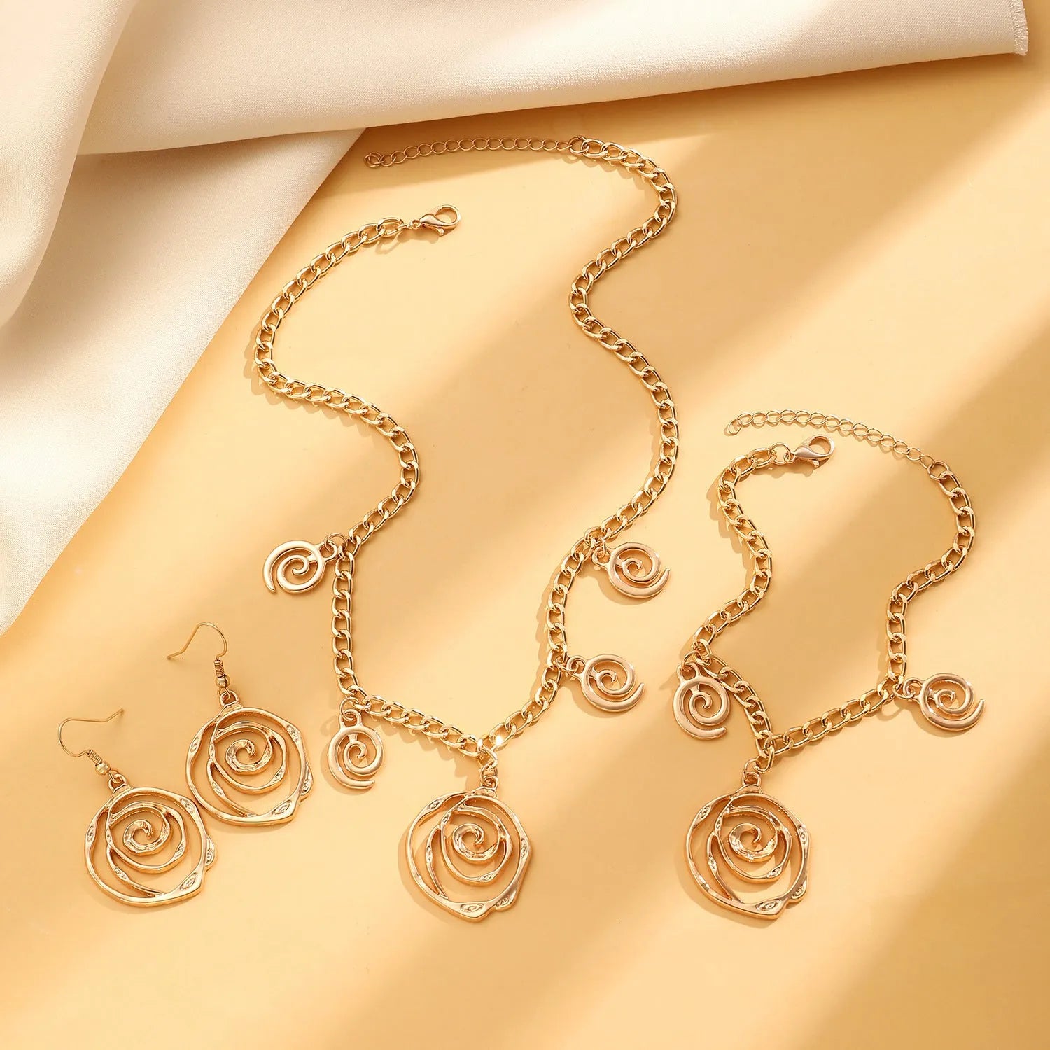 Spiral donut design jewellery set with necklace, bracelet and ear hooks in gold or silver finish