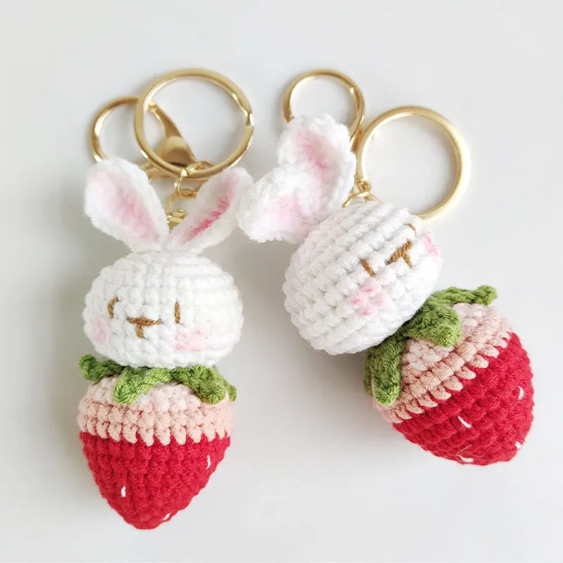 Close-up of a white hand-woven wire pendant showing a rabbit and strawberry cartoon design on a key ring.
