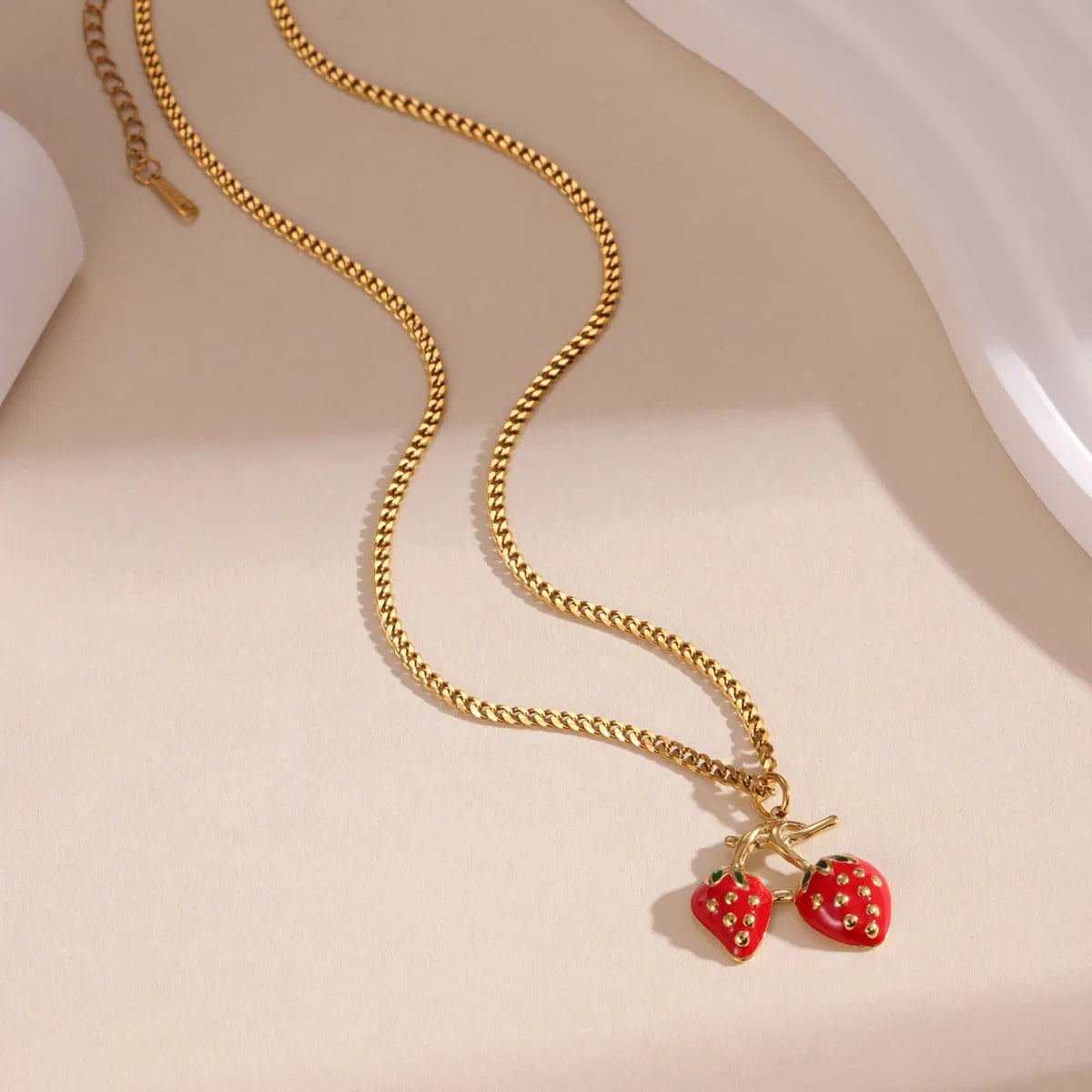 A women's necklace with a detailed strawberry-shaped alloy pendant on a stainless steel chain, shown in red and white gradient colour options.