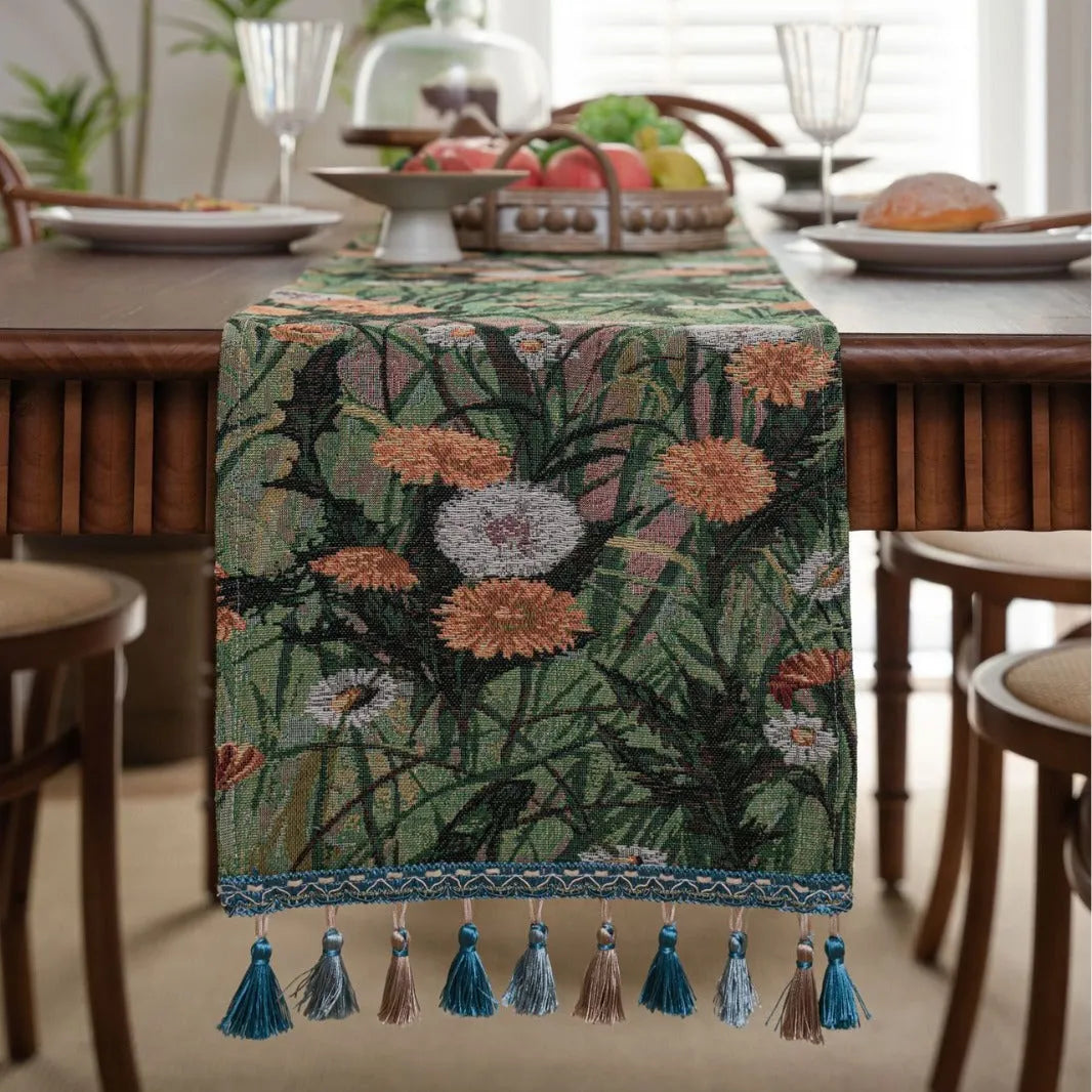 Beige jacquard table runner with flower pattern and long tassels on a wooden dining table.