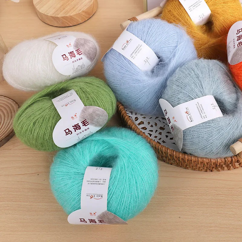 Single 100g ball of mohair yarn in a chosen colour next to a hand-woven light grey scarf sample.