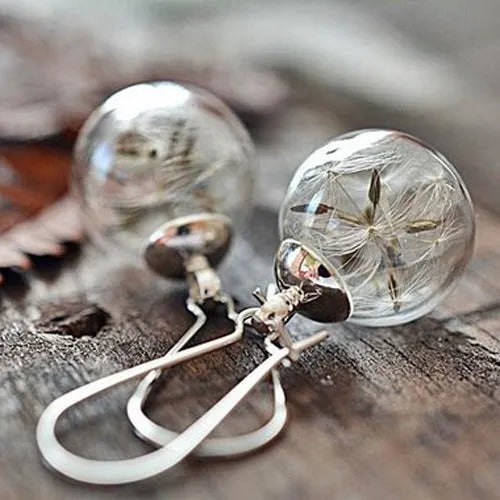 Close-up of transparent glass ball earrings showing a crystal dandelion seed design inside, with silver French hook.