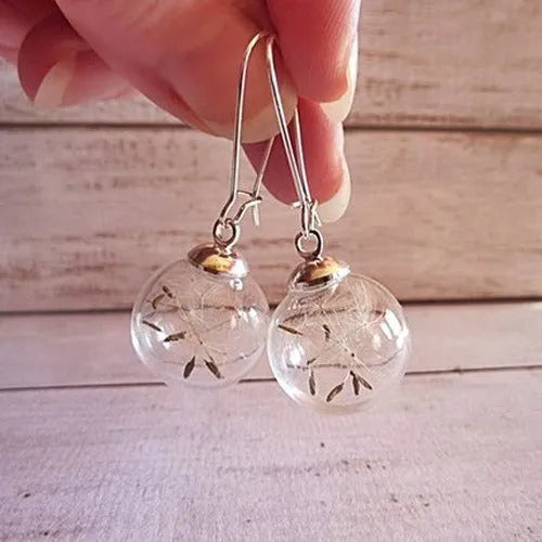Close-up of transparent glass ball earrings showing a crystal dandelion seed design inside, with silver French hook.